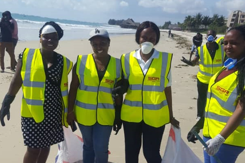 Women posing for photo at the beach while cleaning it